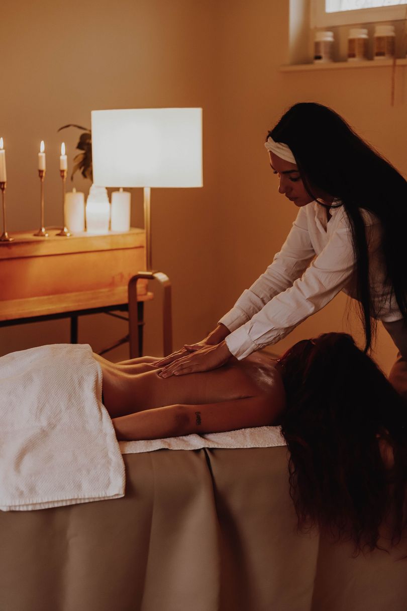 Une masseuse travaille sur les jambes d'un client dans une salle de spa à la lumière tamisée.