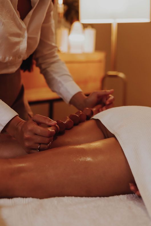 Une esthéticienne effectue un massage du dos aux pierres chaudes sur une cliente couverte d'une serviette.