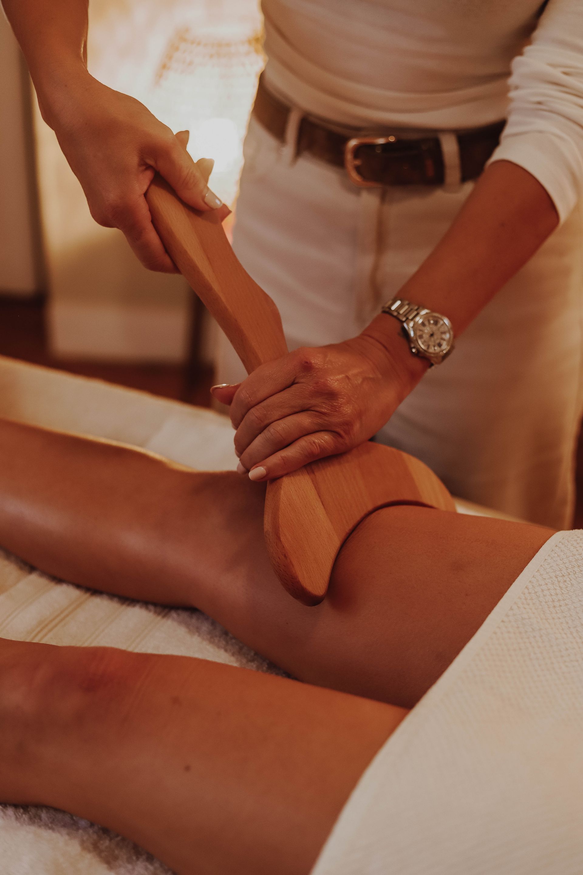 Mains utilisant un outil de massage en bois sur la jambe d'une personne lors d'un soin au spa.