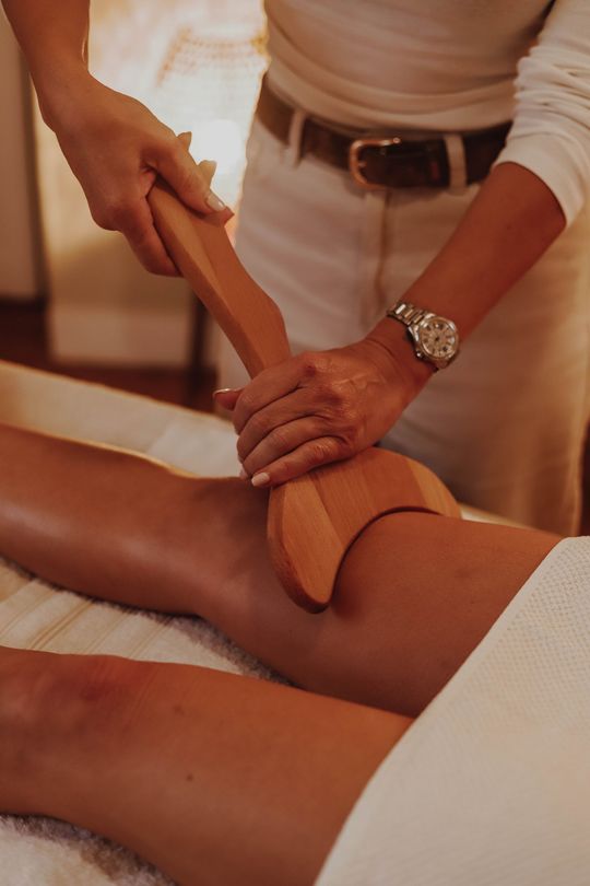 Un massothérapeute utilise un outil en bois sur la jambe d'une cliente lors d'un soin au spa.