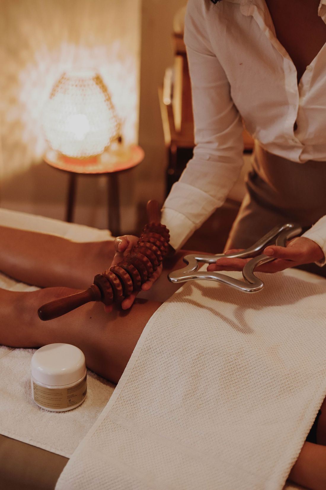 Une masseuse applique des pierres chaudes sur le dos d'un client, enveloppé dans une serviette, dans une salle de spa à l'ambiance tamisée.