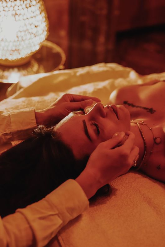 Une personne allongée sur un lit, le visage délicatement tenu par quelqu'un d'autre, dans une chaude lumière orangée.