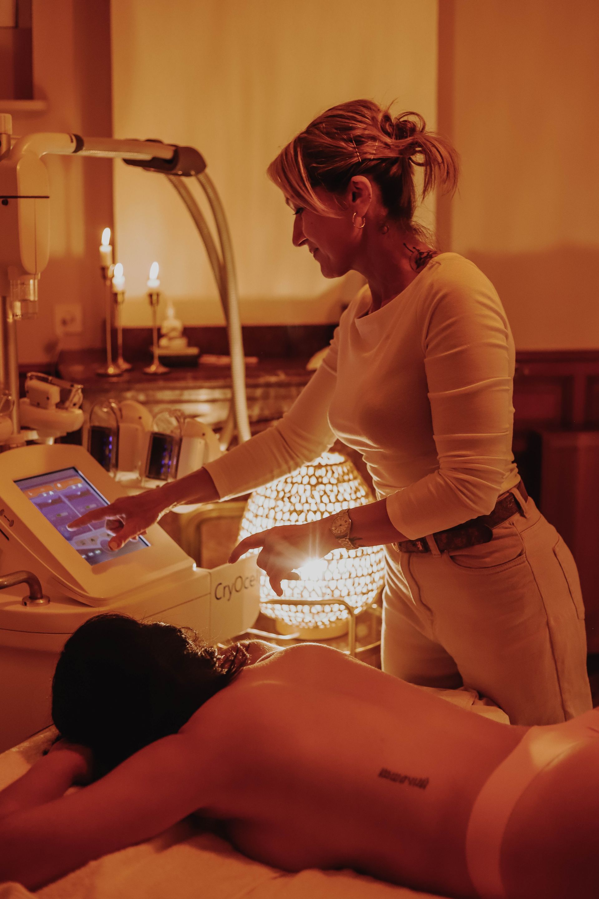 Une esthéticienne utilise un appareil lumineux sur une cliente dans une salle de soins chaleureuse et tamisée.