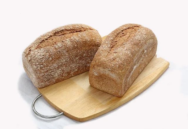 Dos hogazas de pan están colocadas sobre una tabla de cortar de madera.