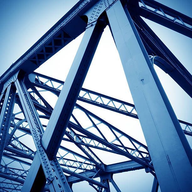Estructura de puente de acero azul contra un cielo brillante, que muestra intrincadas vigas de soporte y remaches.