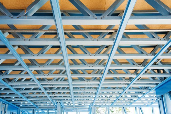 Las vigas de acero azules del techo forman una cuadrícula con paneles de madera, probablemente la estructura del techo o del piso de un edificio.