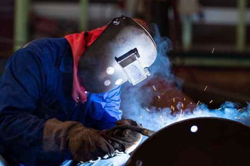 Soldador con mono azul y máscara protectora, trabajando con chispas en un taller.