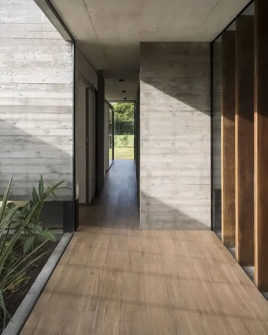 Un pasillo moderno con paredes de hormigón texturizado, suelo de madera y un corredor.