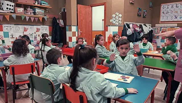 Un grupo de niños están sentados en mesas en un aula.