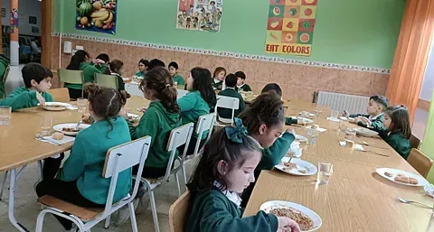 Un grupo de niños están sentados en mesas en un aula comiendo comida.