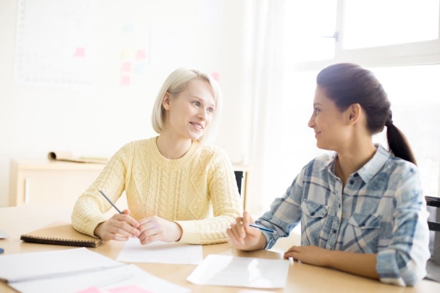 Dos mujeres están sentadas en una mesa hablando entre sí.