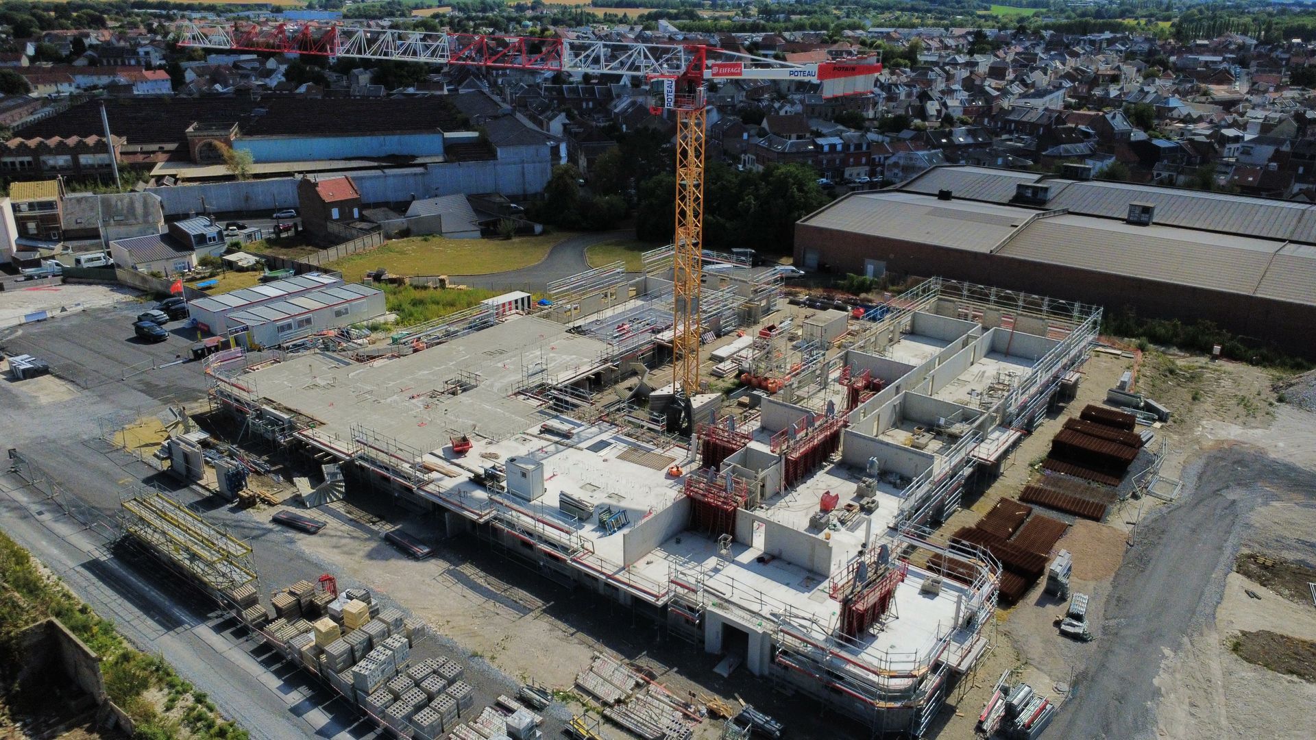 Vue aérienne d'un chantier de construction avec une grande grue et des bâtiments inachevés.