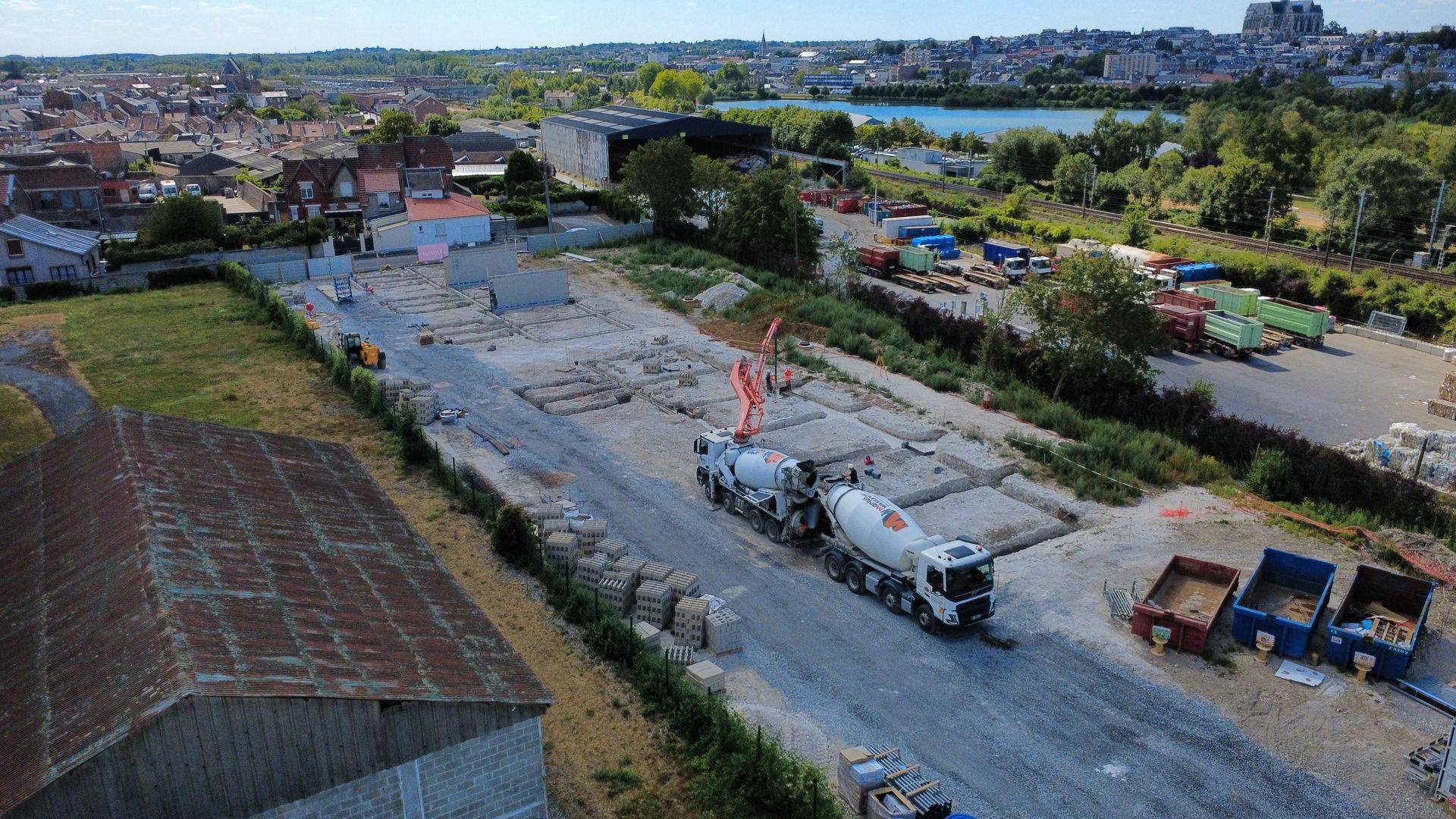 Vue aérienne d'un chantier de construction avec des excavatrices, des camions et un pont en arrière-plan.