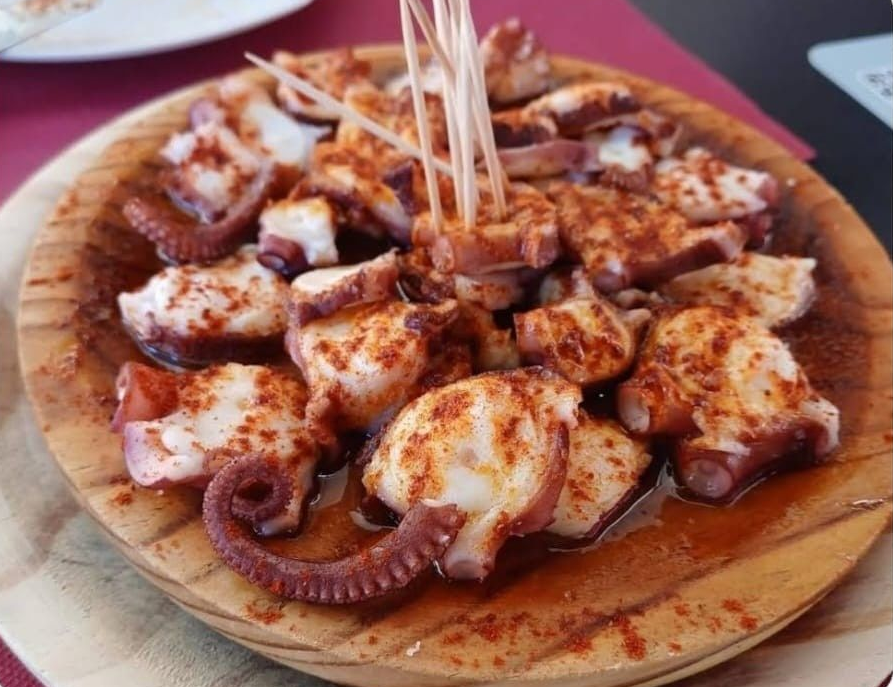 Pulpo a la gallega servido en un plato de madera tradicional con palillos, sazonado con pimentón y aceite de oliva.