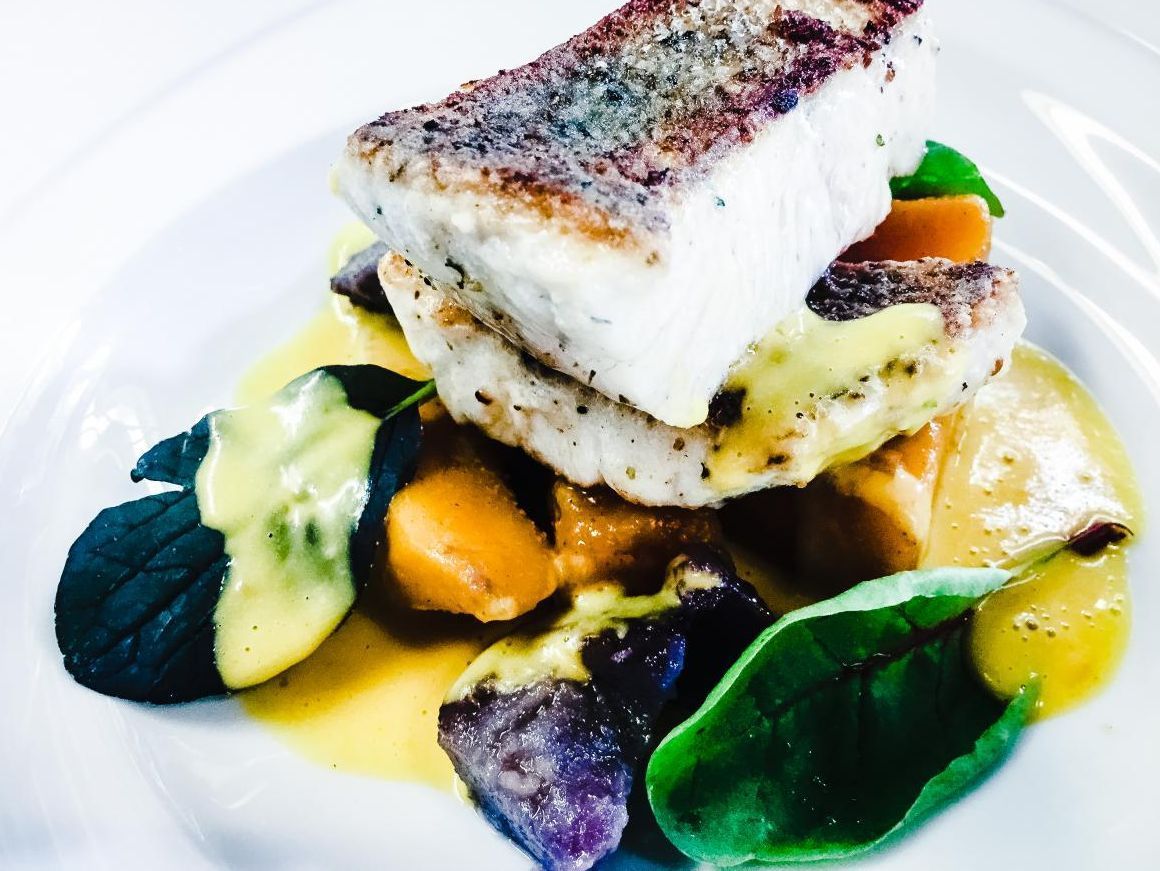 Ein weißer Teller mit einem Stück Fisch und Gemüse