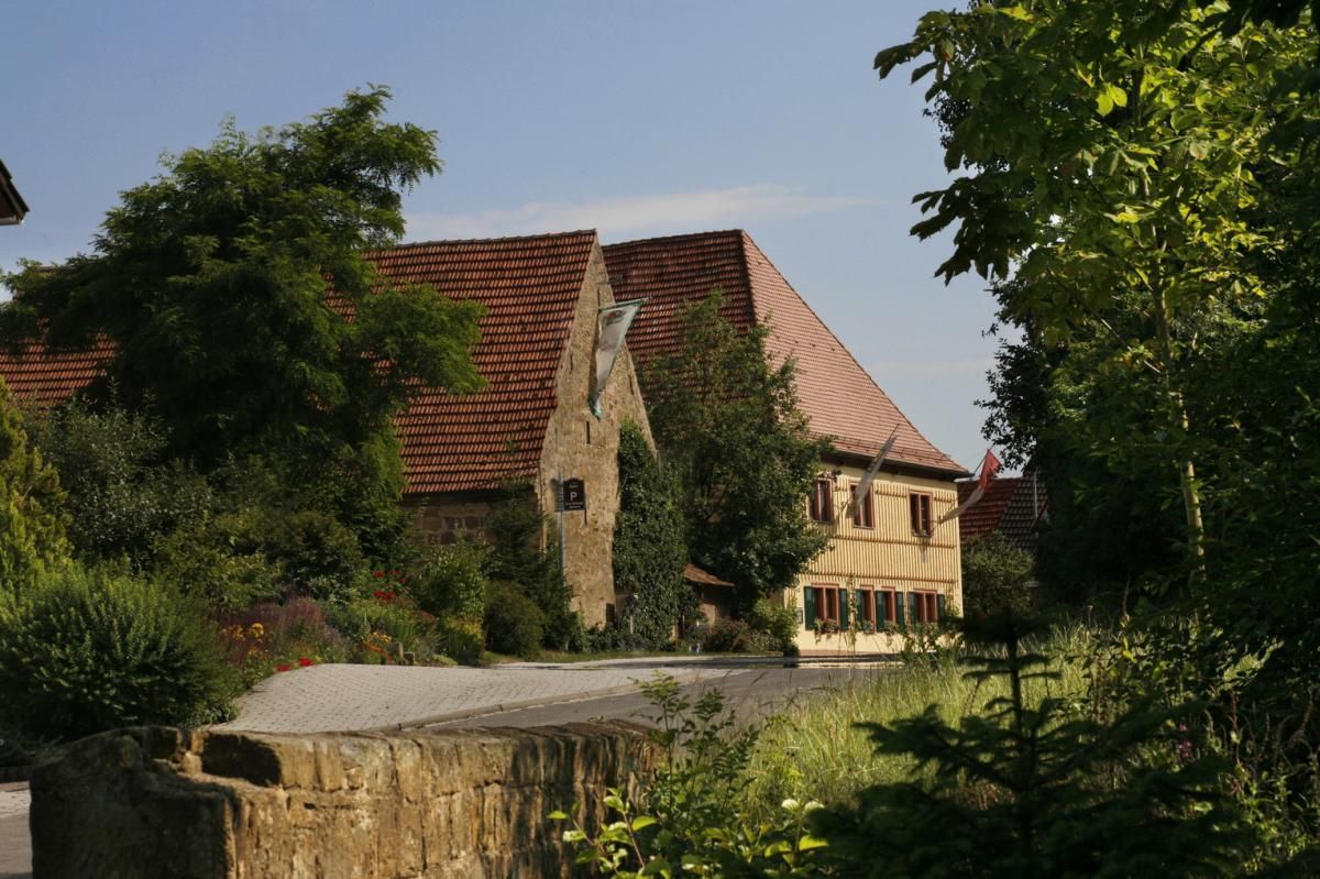 Ein Haus mit einem roten Ziegeldach ist von Bäumen und Büschen umgeben.