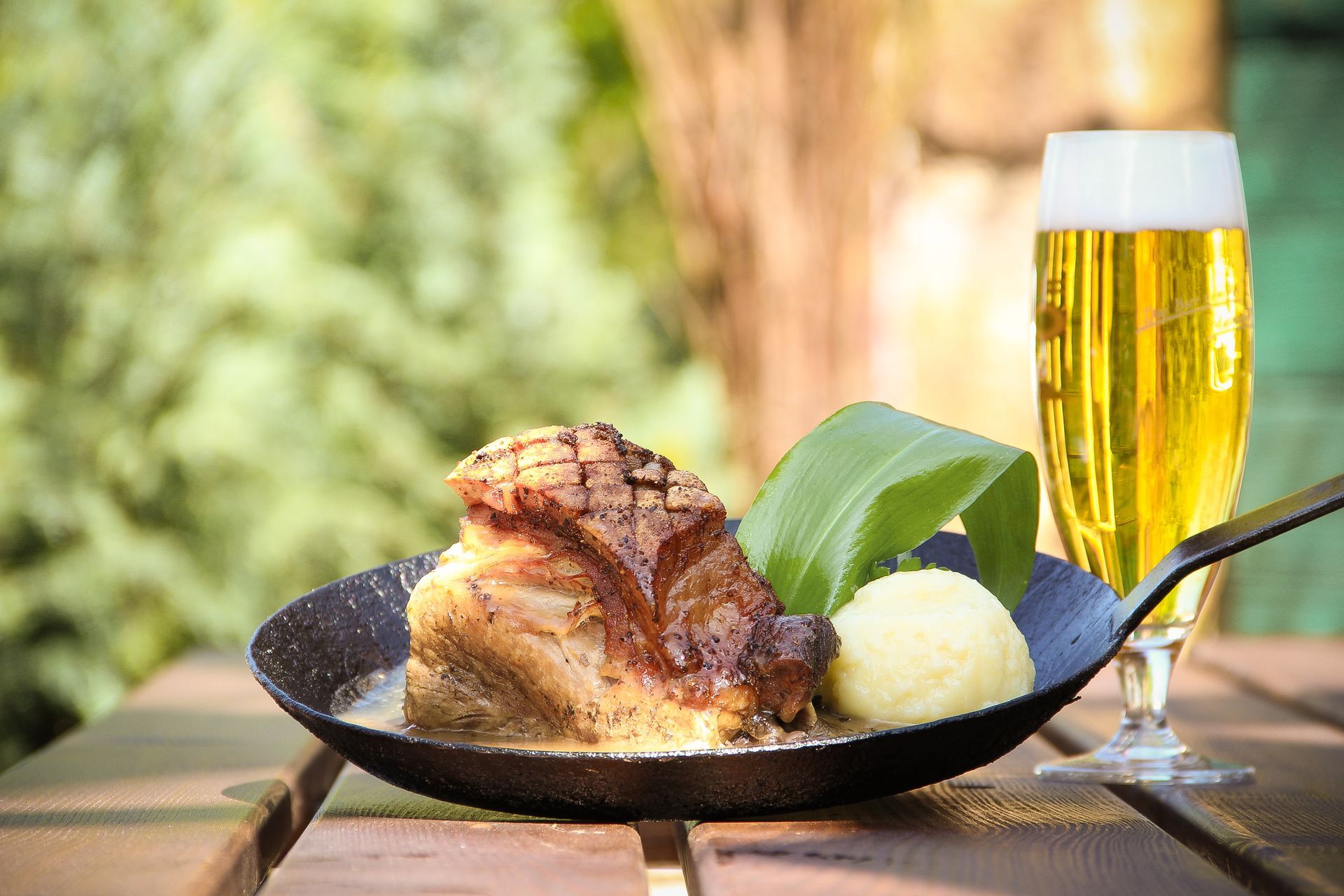 Pfanne mit gebratenem Fleisch, Knödel, Bier; Tischgedeck im Freien.