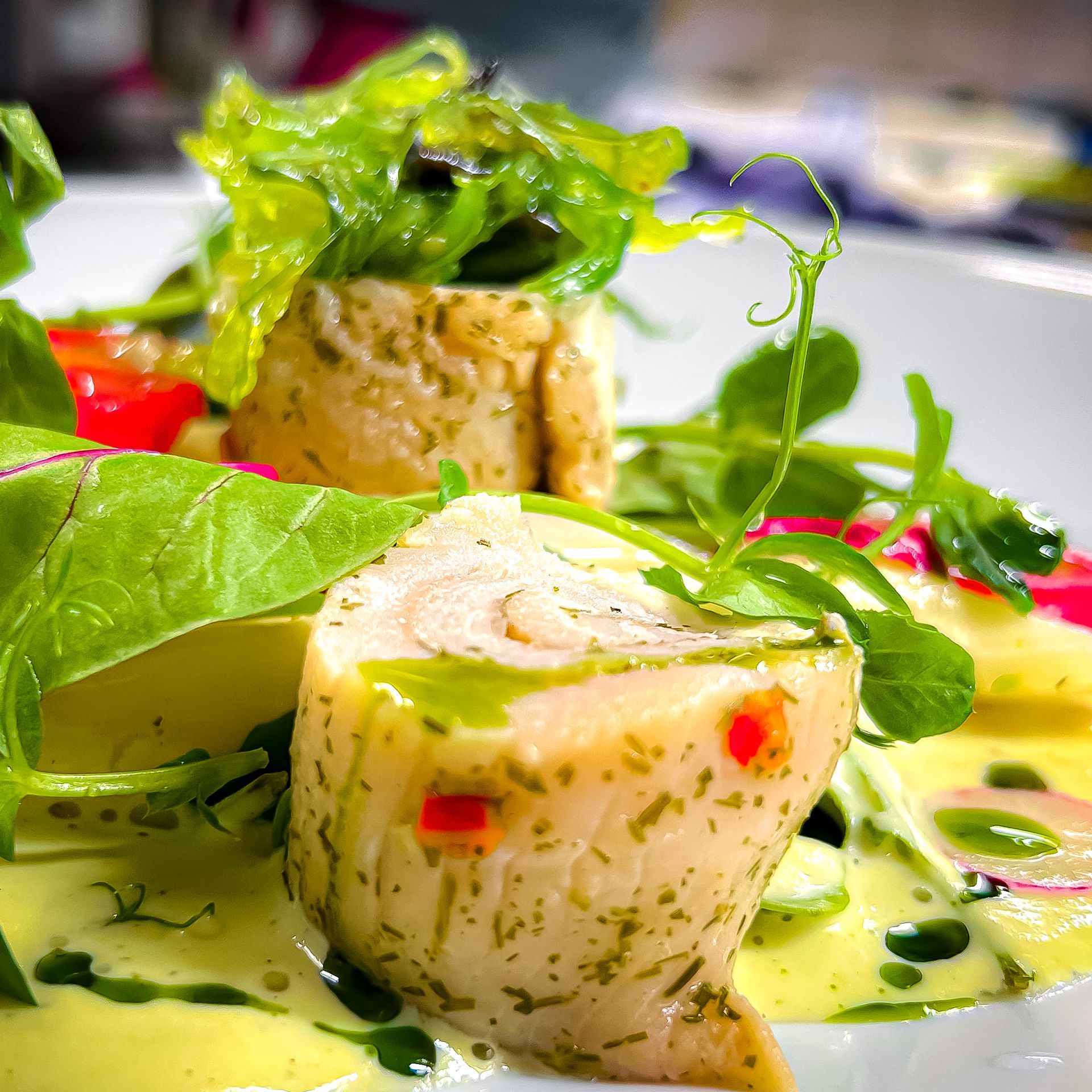Nahaufnahme eines Gourmetgerichts: gerollter Fisch mit Kräutern und Gemüse auf einem Teller.