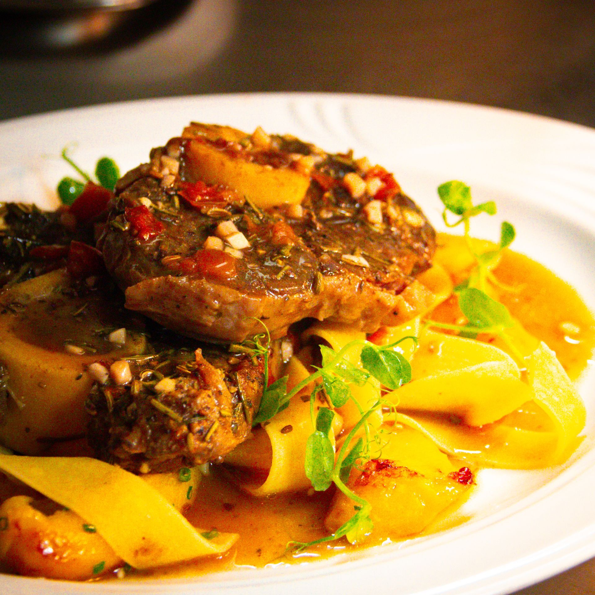 Ossobuco mit Nudeln und Sauce auf einem weißen Teller, garniert mit Kräutern.
