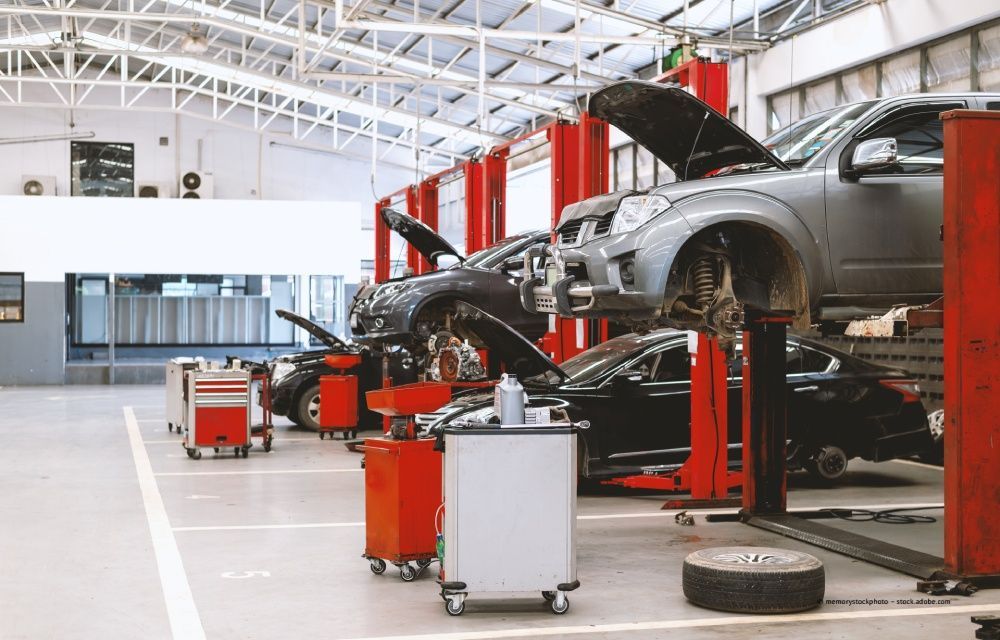 Karosserien auf Hebebühnen in einer hellen Autowerkstatt, Werkzeuge und Wagen in der Nähe.