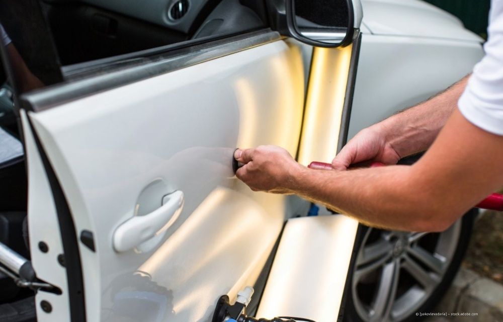 Ein Mechaniker benutzt rote Starthilfekabel, um in einer Werkstatt einen Automotor zu reparieren.