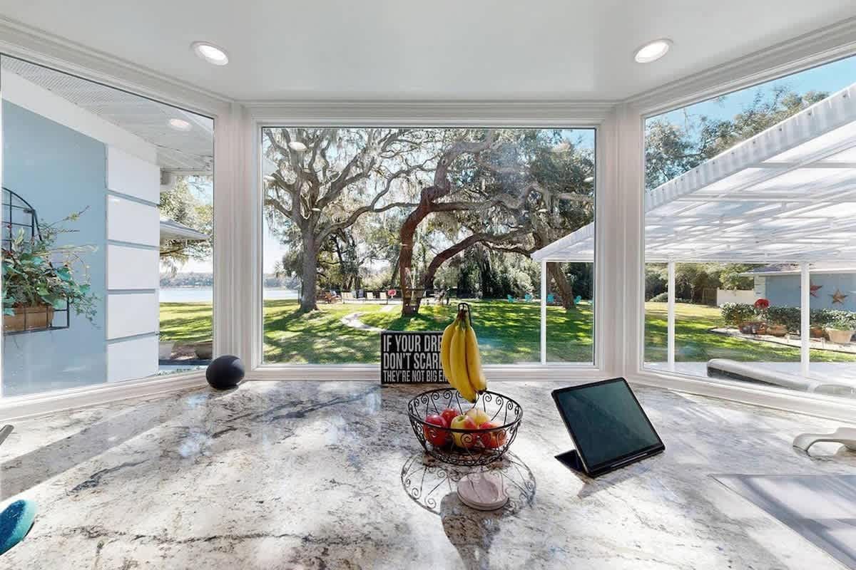 Kitchen with large windows overlooking a yard and lake. Fruit basket, banana, and laptop on the granite countertop.