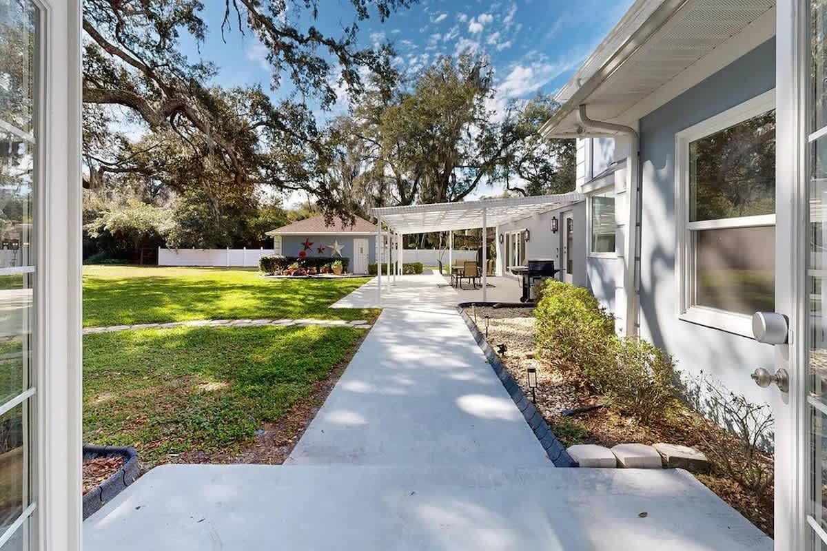 View from French doors of a concrete walkway and yard, leading to a patio and building.
