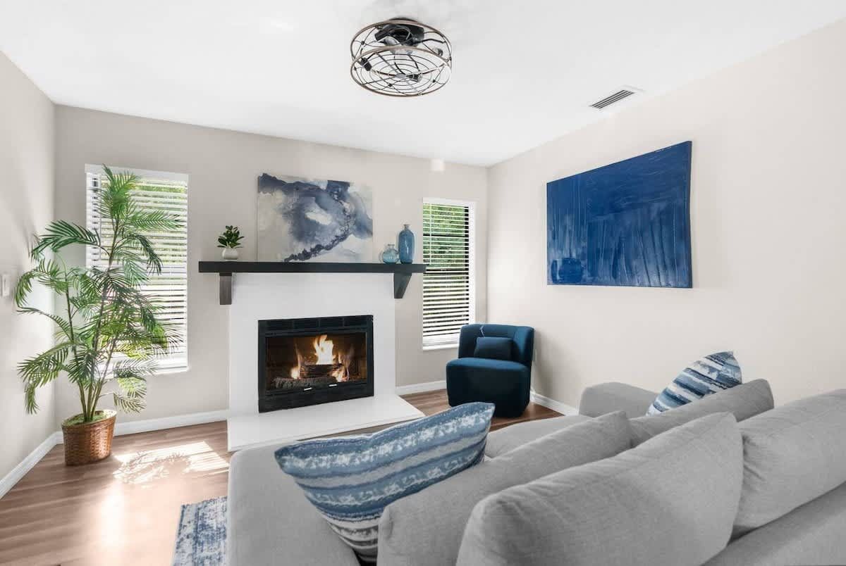 Living room with fireplace, gray sofa, blue artwork, and potted plant.