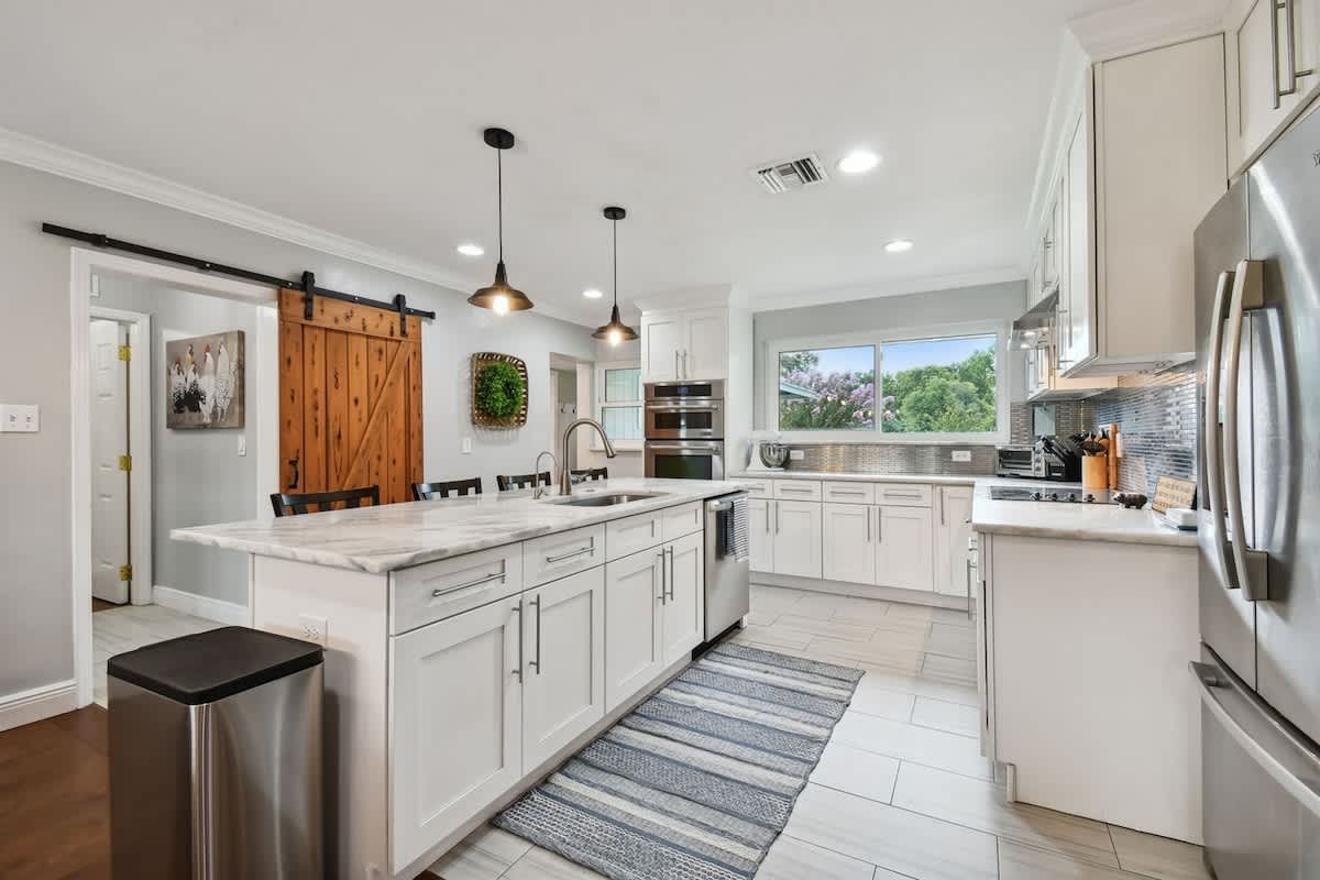 Bright kitchen with white cabinets, island, stainless steel appliances, and a rustic wooden sliding door.