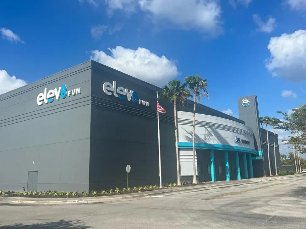 Exterior view of Elev8 Fun building with blue and gray facade, palm trees, and blue sky.