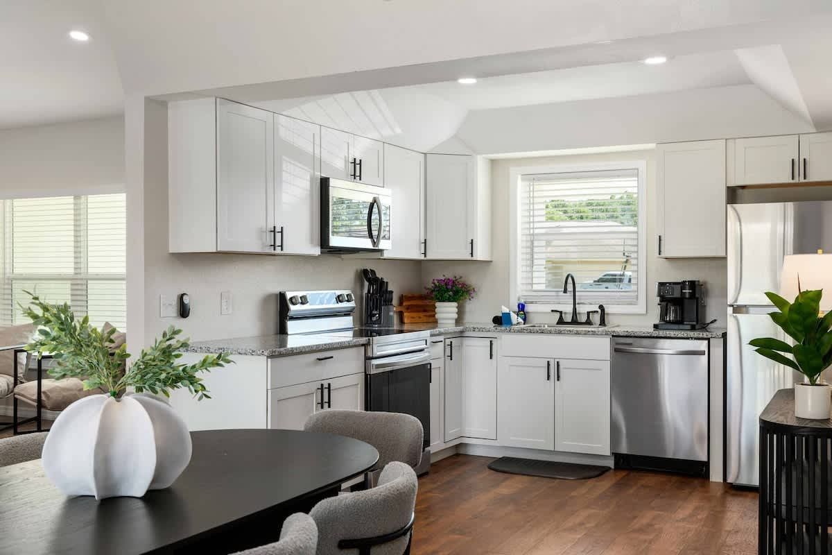 Modern white kitchen with stainless steel appliances, open to a dining area.