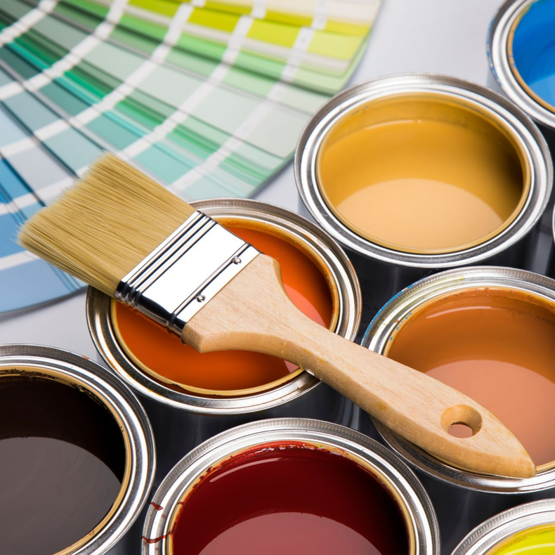 Des pots de peinture avec des nuanciers colorés et un pinceau posé dessus.