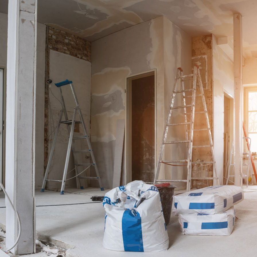 Pièce baignée de soleil en cours de rénovation, avec des échelles, des outils et des matériaux de construction éparpillés sur le sol.