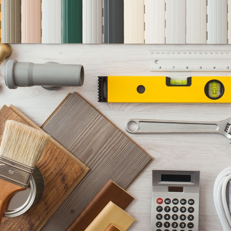 Vue de dessus d’outils de rénovation, d’échantillons de peinture, d’une règle et de papiers peints posés sur un plan de travail.
