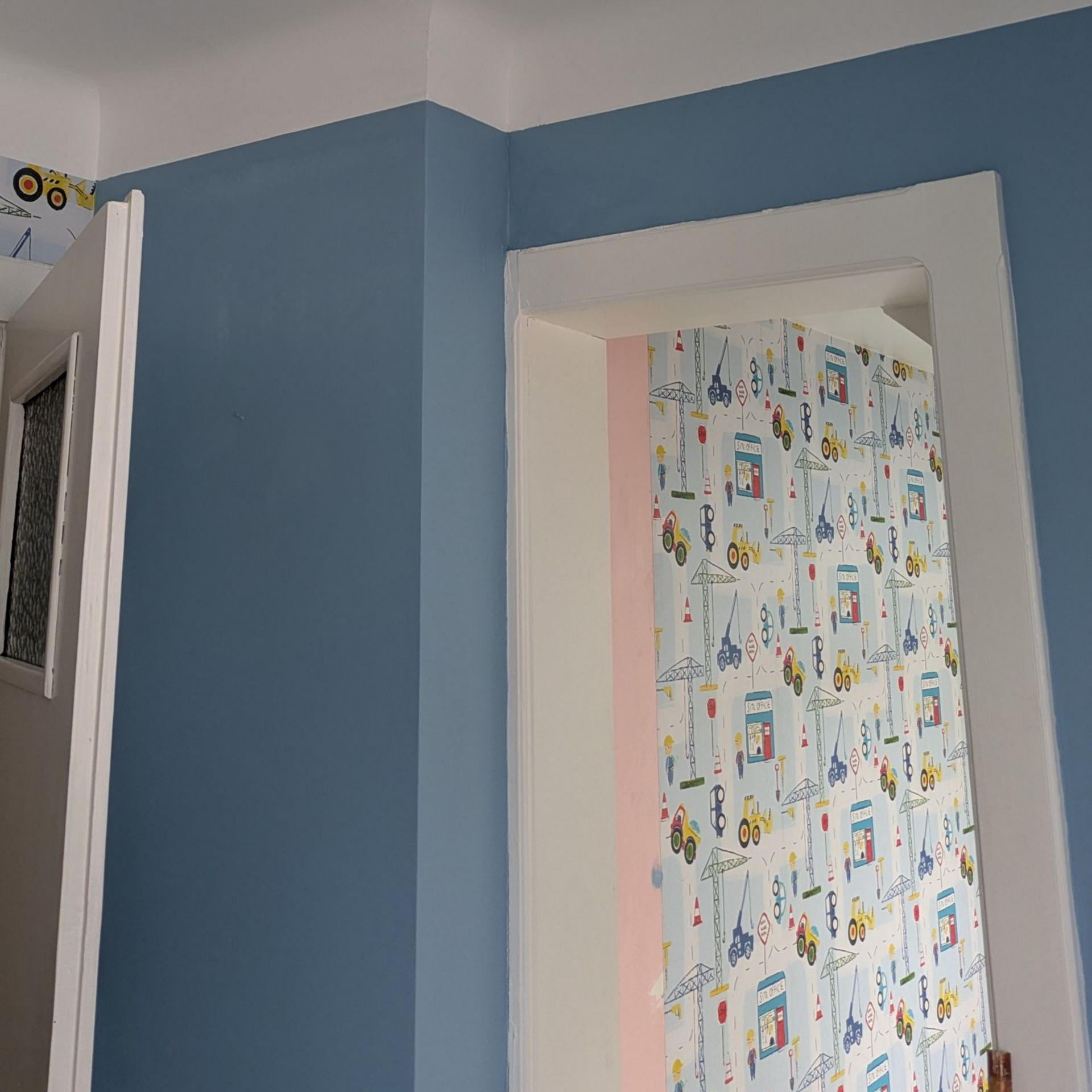 Couloir bleu avec des moulures blanches et une porte donnant sur une pièce au papier peint coloré à motifs.