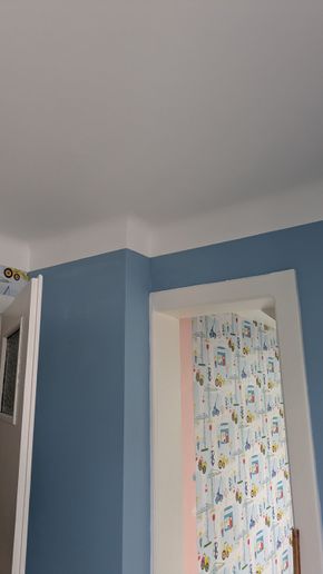 Murs bleus et moulures blanches dans une pièce avec une porte et du papier peint à motifs au-delà.