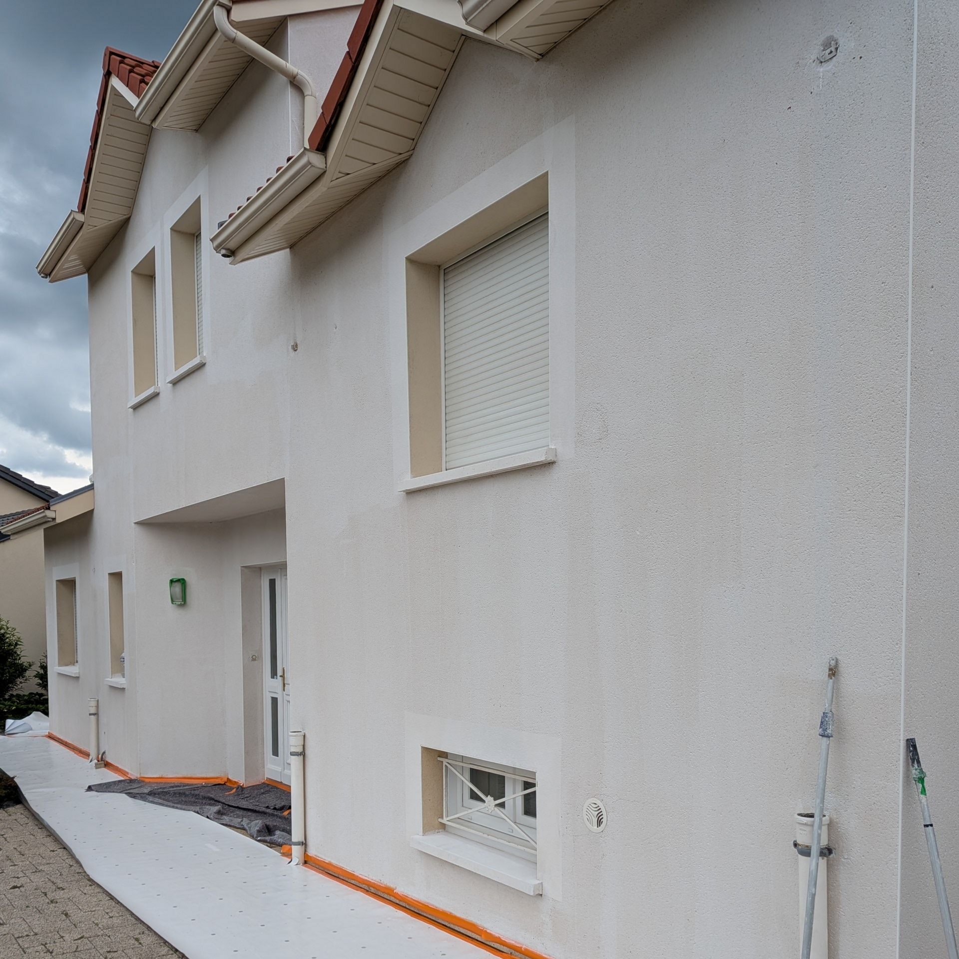Extérieur d’une maison blanche aux garnitures orange, avec du matériel de peinture et une allée en gravier.