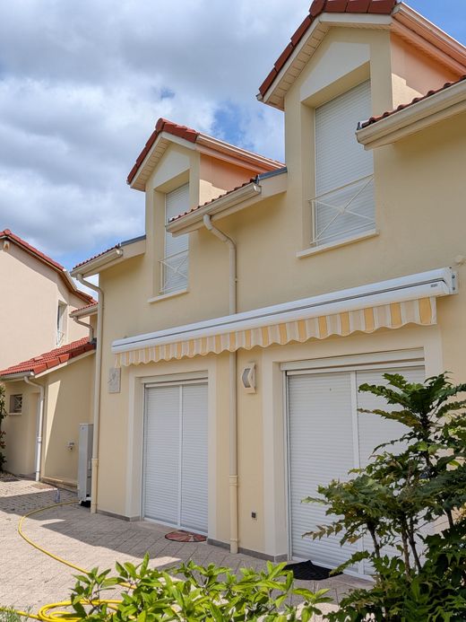 Maisons de ville en stuc beige, aux volets et aux stores blancs, sous un ciel nuageux.