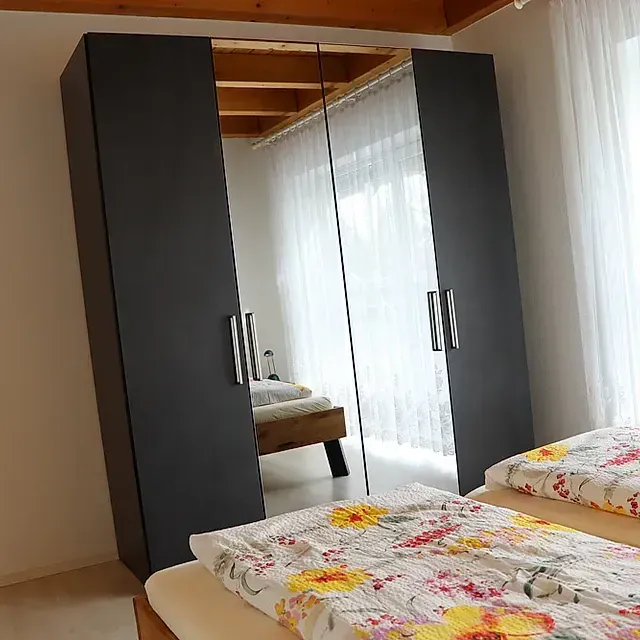 Dunkelgrauer Kleiderschrank mit Spiegeltüren, zwischen zwei Betten.