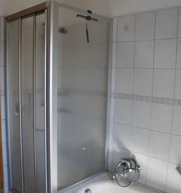 Duschkabine mit faltbarer Milchglastür und weiß gefliesten Wänden.