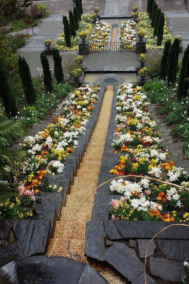 Steinstufen und ein mit bunten Blumen gesäumter Wasserkanal in einer Gartenanlage.