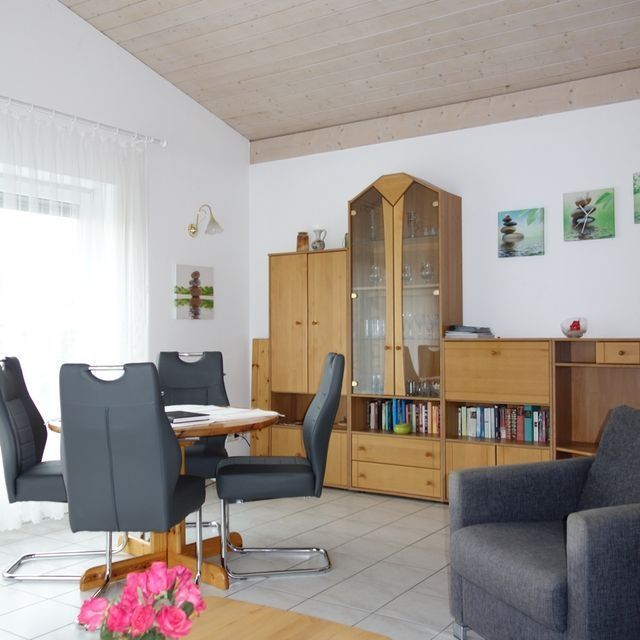 Wohnzimmer mit Holzmöbeln, rundem Tisch, grauen Stühlen und Kunstwerken an den Wänden.
