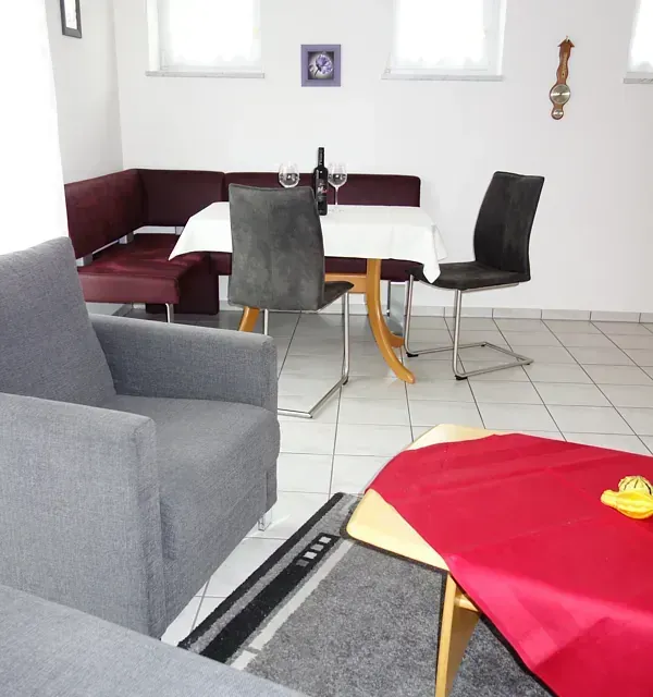 Wohnzimmer mit Esstisch, Sitzgelegenheiten und einem rot bezogenen Couchtisch.