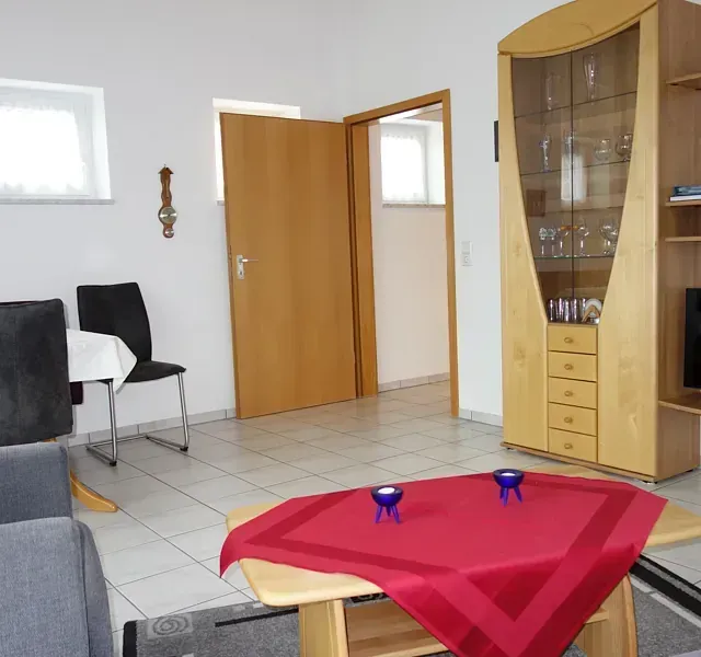 Wohnzimmer mit Möbeln, darunter ein Tisch, Stühle und eine Vitrine.