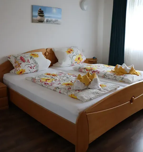 Schlafzimmer mit zwei Betten, geblümter Bettwäsche, Holzrahmen, Nachttischen, Wandbildern und einem Vorhang.