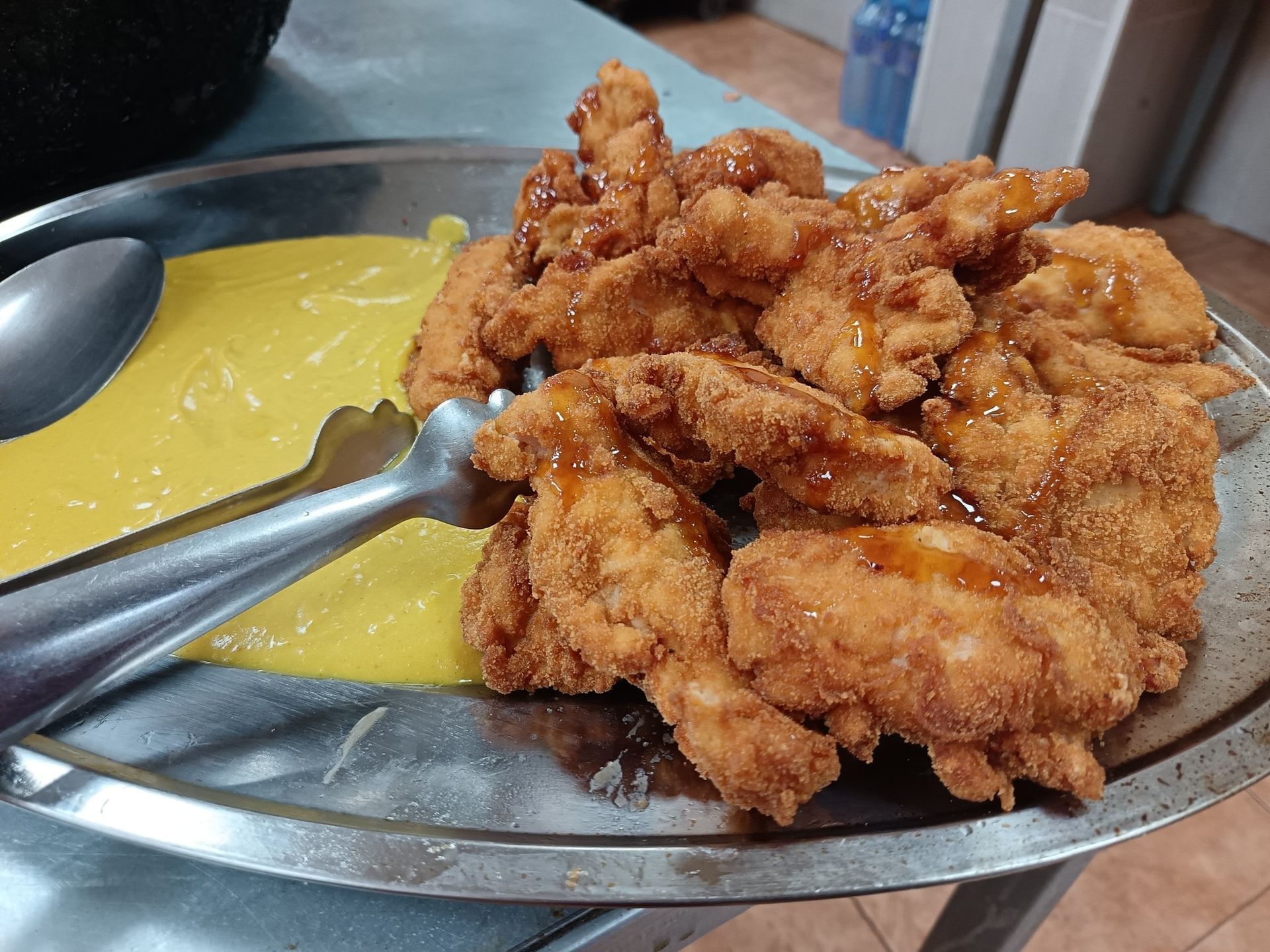 Un plato de pollo frito y salsa amarilla con pinzas.