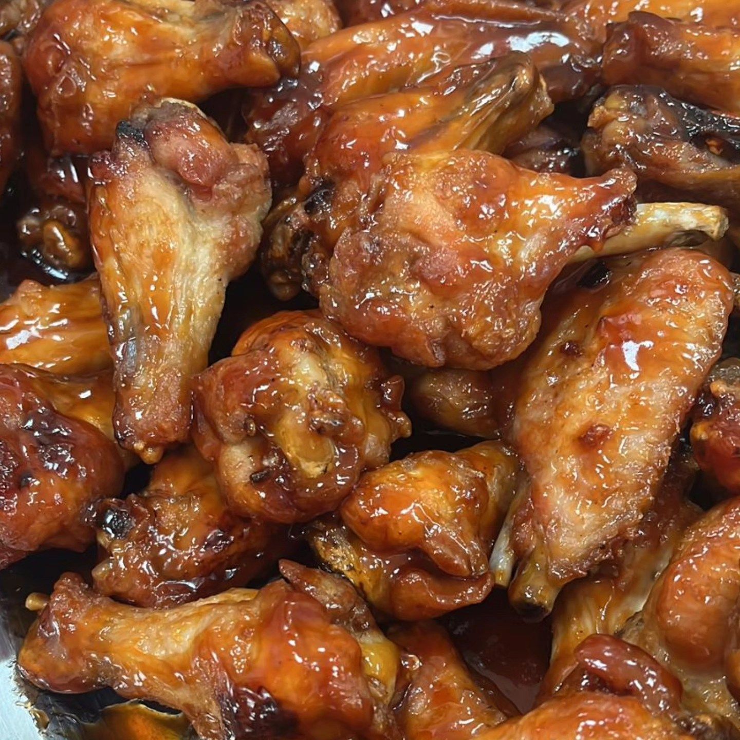 Un primer plano de una pila de alitas de pollo con salsa encima.