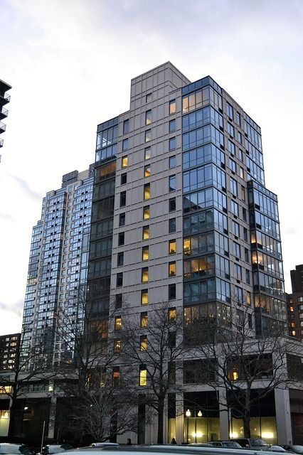 Un edificio de apartamentos alto y moderno, con balcones de cristal y una fachada de color claro, visto desde el nivel de la calle en invierno.
