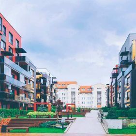 Un moderno complejo de apartamentos con un paseo peatonal y zonas verdes entre los edificios bajo un cielo nublado.