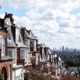 Una hilera de casas tradicionales de ladrillo con frontones puntiagudos, con vistas al horizonte de una ciudad lejana bajo un cielo azul nublado.
